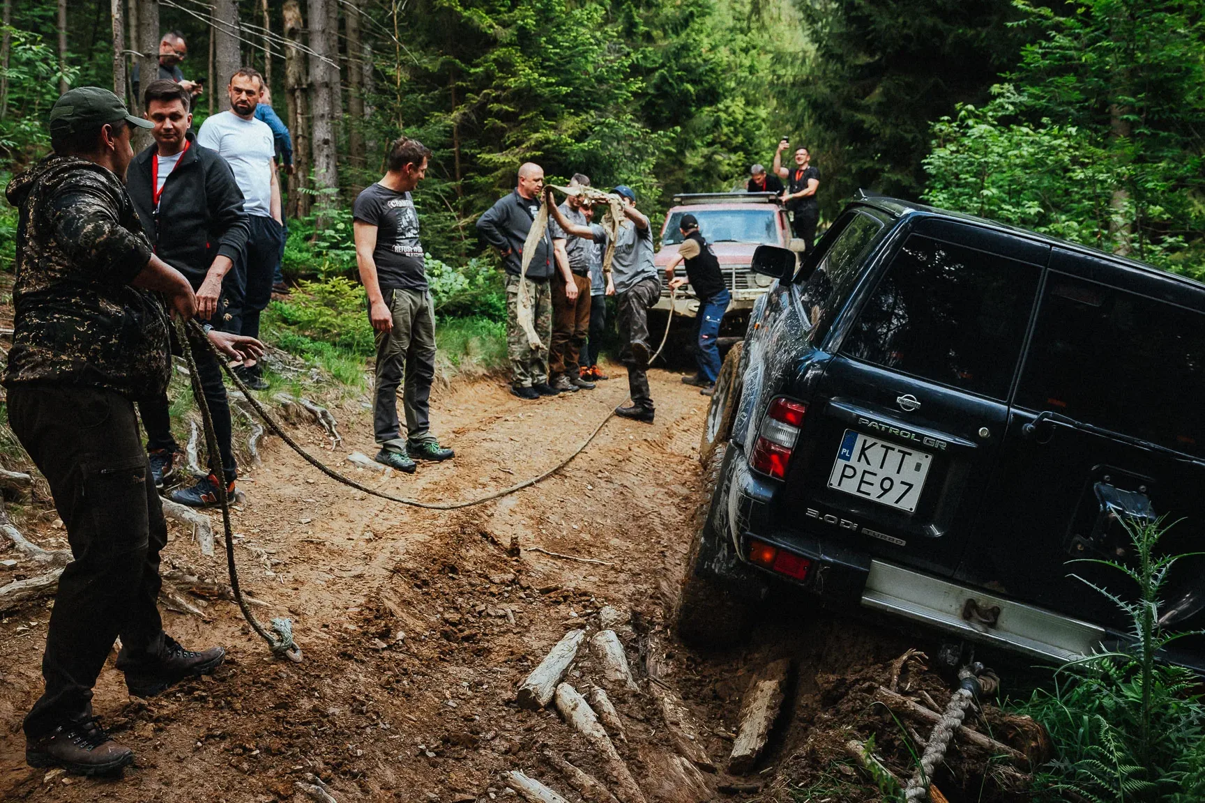 Participants on a corporate trip pulling an off-road vehicle out of the mud during an off-road drive in the forest