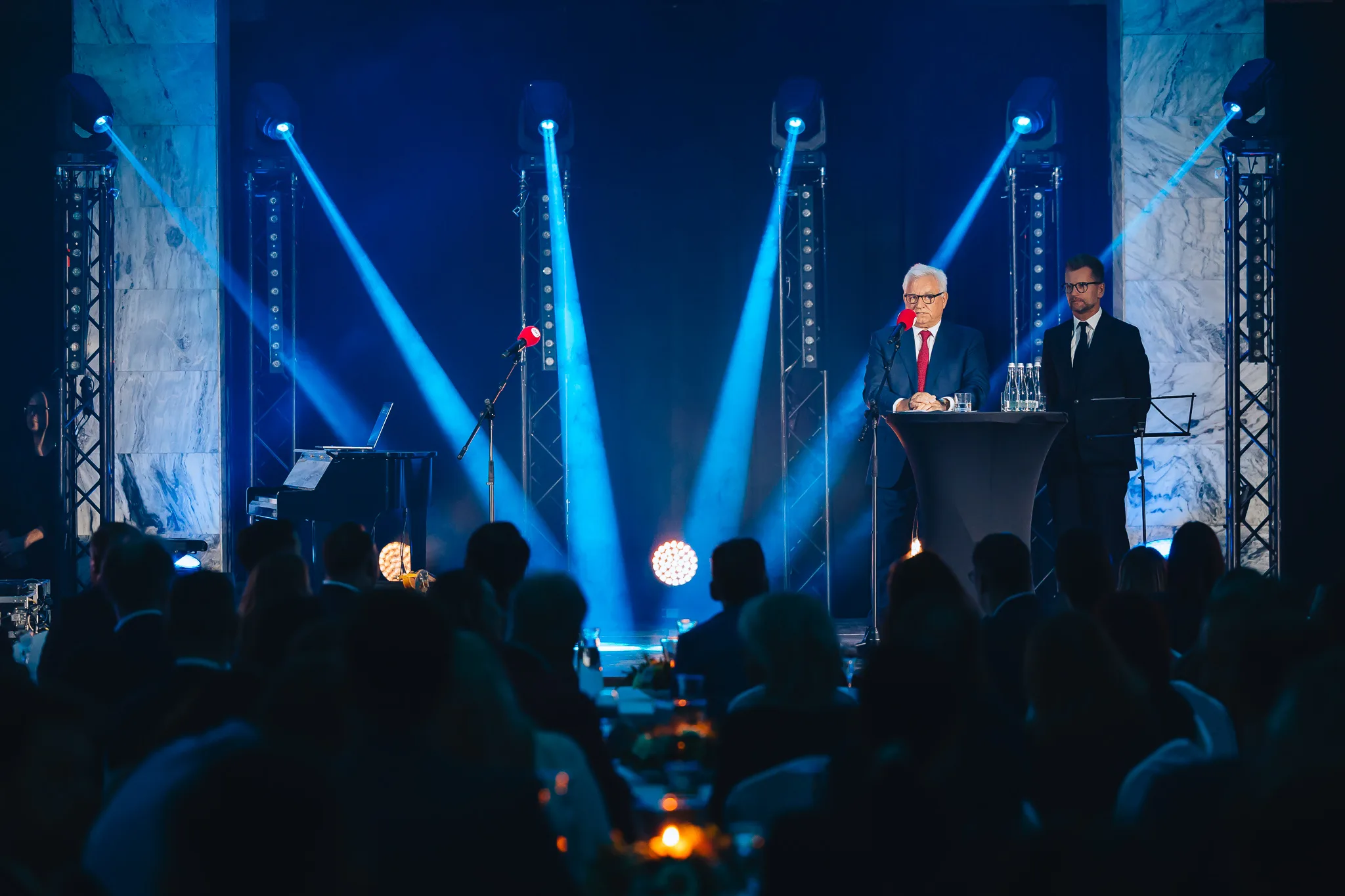 A speech on the stage at an evening gala, beams of spotlights in a dark hall and the silhouettes of guests in the foreground