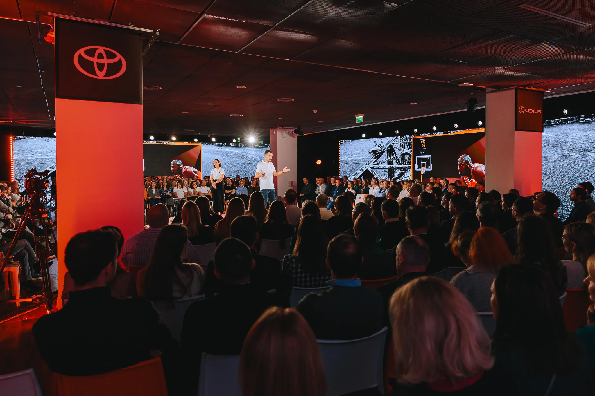Speakers on stage at a corporate conference in Warsaw and a full auditorium of attendees, a wide shot from behind the audience