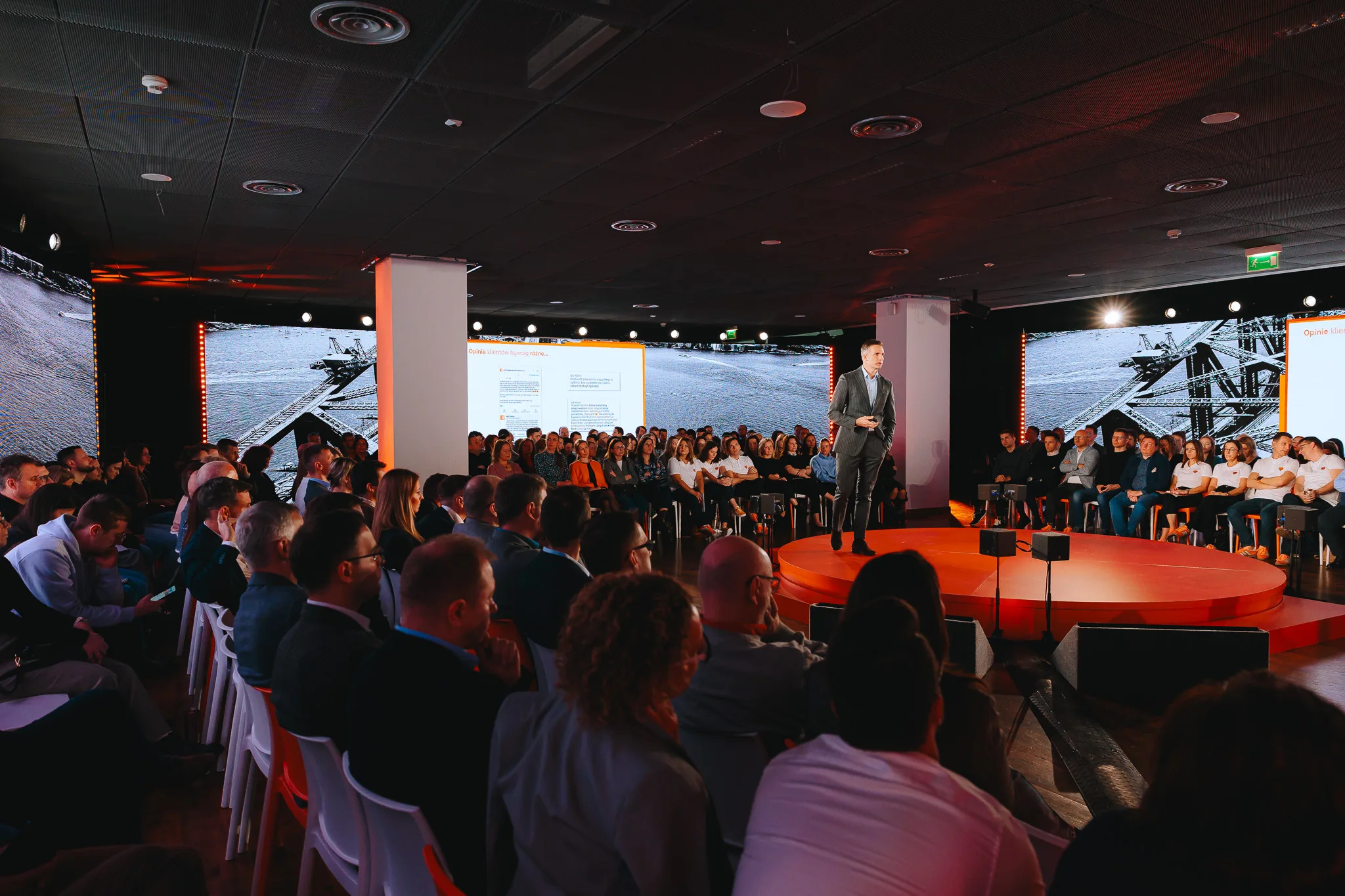 A speaker on a circular stage surrounded by the audience during a corporate conference in Warsaw