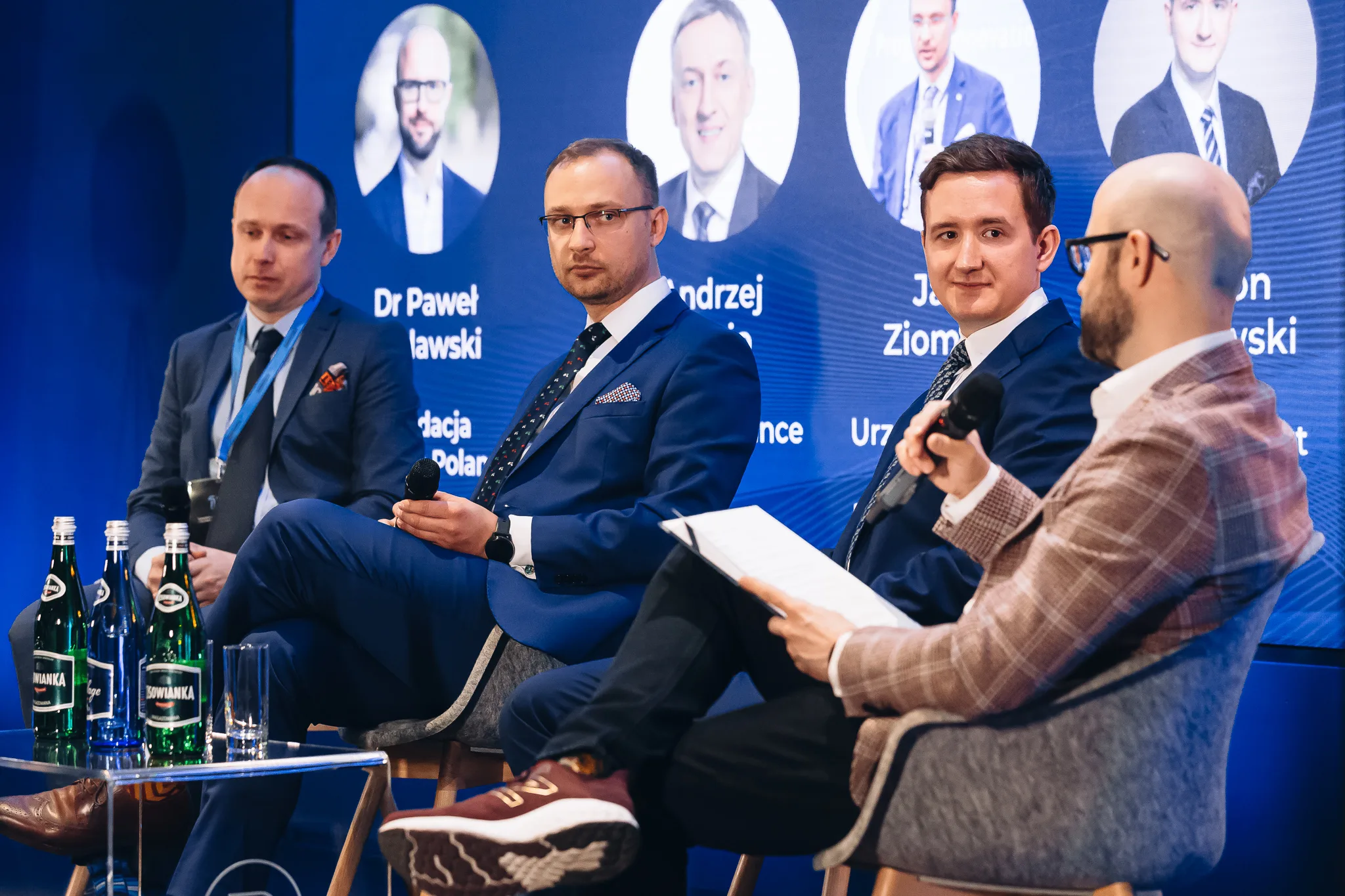A panel discussion at a conference in Warsaw, with four participants on the stage and a moderator with a microphone and sheets of questions