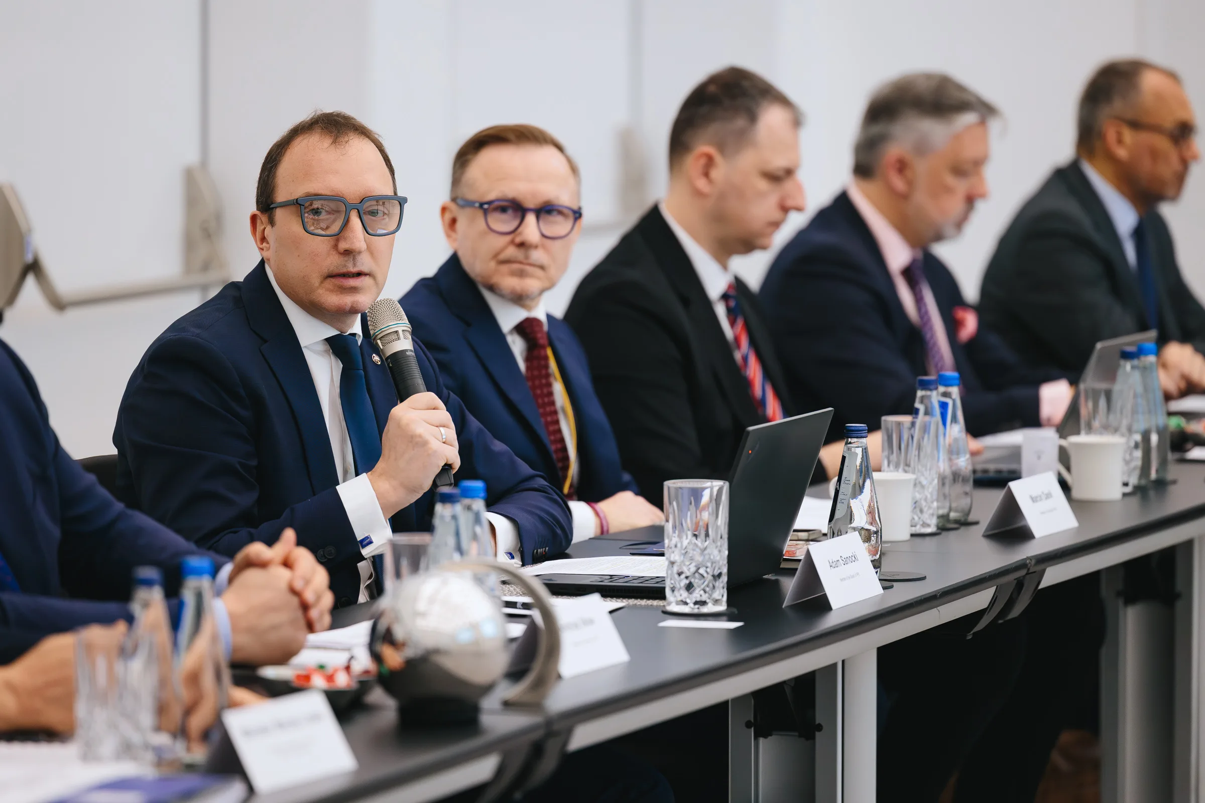 A close-up of a speaker with a microphone during a conference in Warsaw; panellists at the main table