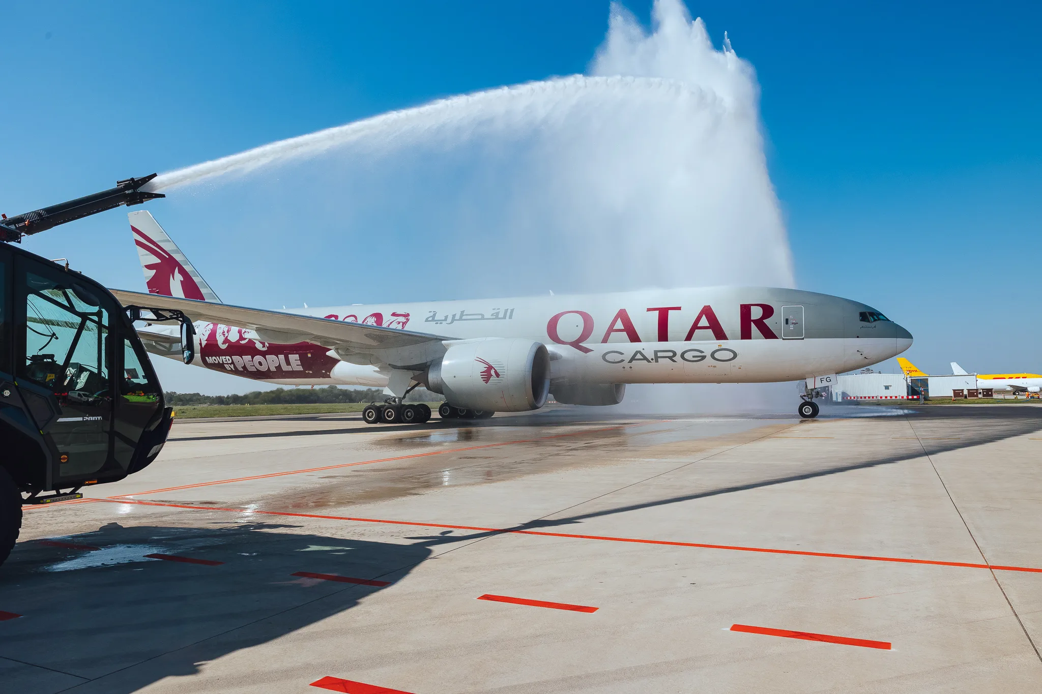 A cargo aircraft under a water salute from airport fire engines on the apron, welcoming the new aircraft